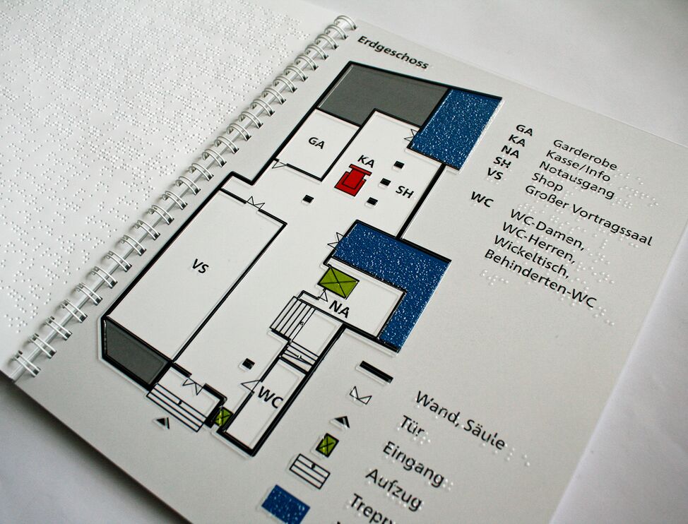 Aufgeschlagene Broschüre mit taktilem Grundriss und Legende (Erdgeschoss)